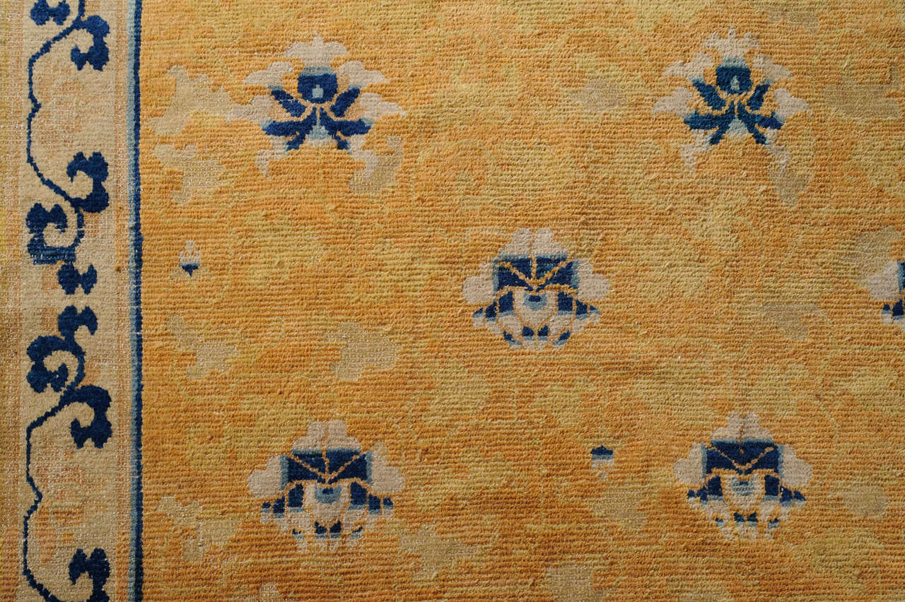 A rare and beautiful early Chinese carpet characterized by an infinite repeat of parallel and offset rows of blue and ivory lotus blossoms, symbols of purity, on a two-tone yellow background. The archaic, somewhat angular style of drawing, seen here